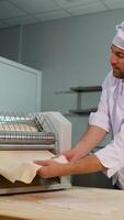 Professional chef in a white uniform placing a sheet of dough into a dough sheeter machine for flattening in restaurant video
