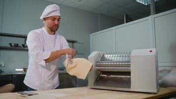 Professional chef in a white uniform placing a sheet of dough into a dough sheeter machine for flattening in restaurant video