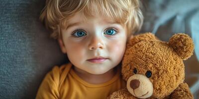 Young child with curly hair holding a teddy bear while lying on a cozy bed in a softly lit room photo