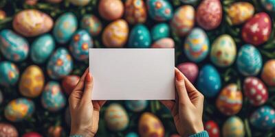 Colorful Easter eggs arranged on grass with a blank card held by hands in a festive spring setting during daytime photo