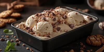 Creamy dessert featuring vanilla ice cream with chocolate bits and cookie crumbles on a dark table with garnishing photo
