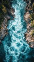 Rushing river flows through rocky canyon surrounded by lush greenery during sunny daylight hours photo