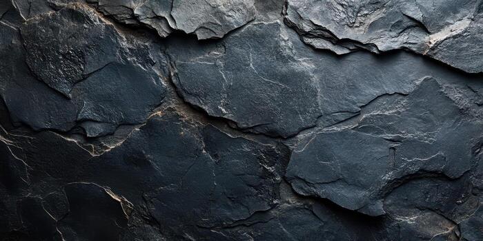 Dark textured rock surface showcasing natural geological patterns and shadows in a dimly lit environment photo