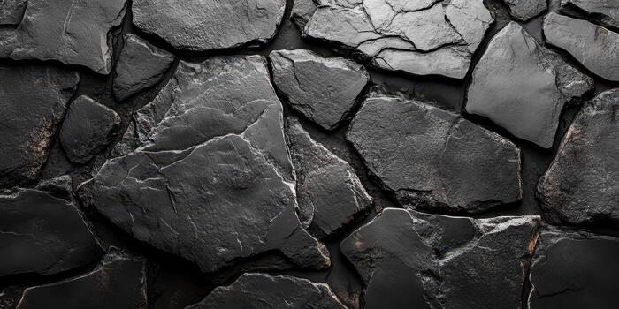 Textured black stone wall with varying shapes and sizes of stones arranged closely together creating an intricate pattern photo
