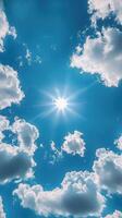 Bright sun shining through fluffy clouds on a clear blue sky during midday photo