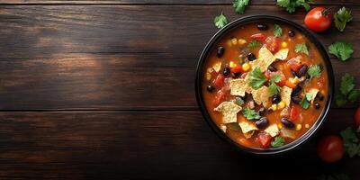 Delicious bowl of hearty black bean soup topped with crunchy tortilla chips and fresh cilantro on rustic wooden table photo