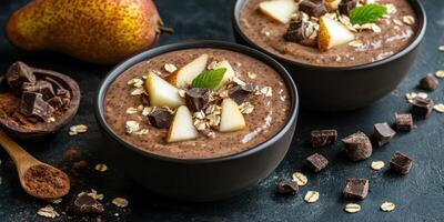 Delicious chocolate chia pudding with fresh pear and chocolate chunks served in black bowls on a dark countertop photo