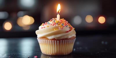 Birthday cupcake with candle and colorful sprinkles illuminated against a dark background photo