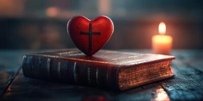 Heart-shaped stone with cross resting on a closed Bible beside a lit candle in a dimly lit room photo