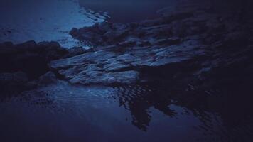 Dark rock formations reflect in calm water during twilight hours video