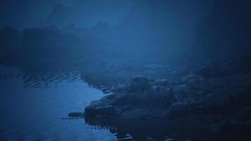 Dark shoreline with rocky formations under a misty blue atmosphere video