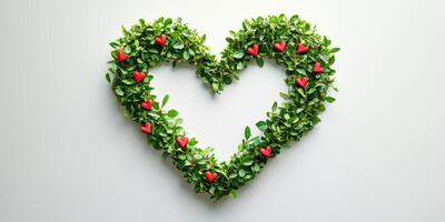 Heart-shaped arrangement made of green leaves and red decorations on a white background photo