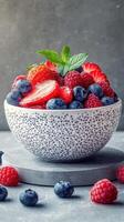 Fresh assortment of colorful berries arranged in a dotted bowl on a textured surface with mint leaves for garnish photo