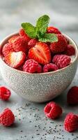 Fresh strawberries and raspberries in a bowl garnished with mint leaves on a textured surface photo
