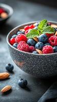 Fresh berries and almonds in a textured bowl garnished with mint leaves in a dark setting photo