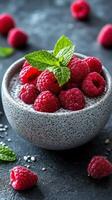 Fresh raspberries topped with mint sit in a speckled bowl on a dark background with scattered ingredients photo