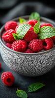 Fresh raspberries with mint leaves in a textured bowl on a dark surface photo