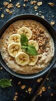 Creamy oatmeal bowl topped with banana slices and mint leaves served with granola and chia seeds photo