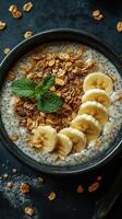 Healthy chia pudding topped with banana slices and granola served in a black bowl photo
