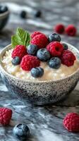 Delicious bowl of creamy yogurt topped with fresh raspberries and blueberries on a marble surface photo