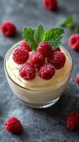 Fresh raspberry dessert served in a clear glass bowl garnished with mint leaves on a dark countertop photo