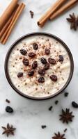 Creamy dessert topped with raisins, spices, and cinnamon in a rustic bowl on a marble surface photo