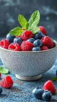 Fresh berries and mint leaves arranged in a decorative bowl on a blue textured surface photo