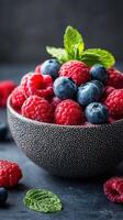 Fresh berries in a textured bowl with mint leaves on a dark background, showcasing vibrant colors and natural freshness photo