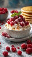 Delicious bowl of cottage cheese topped with fresh raspberries and mint beside fluffy pancakes photo
