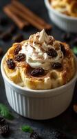 Delicious dessert in a white ramekin topped with whipped cream and raisins, garnished with cinnamon on a dark surface photo