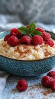 Delicious bowl of creamy rice pudding topped with fresh raspberries and mint on a gray textured background photo