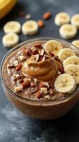 Healthy chocolate chia pudding topped with banana slices, nut butter, and almonds in a clear bowl on a dark surface photo