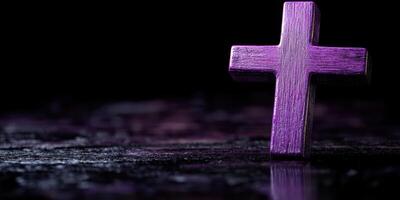 Purple wooden cross positioned on a dark surface with soft light highlighting its texture at dusk photo