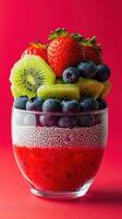 Colorful fruit dessert in a glass with vibrant strawberries, blueberries, kiwi, and chia seeds on a red background photo