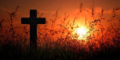 Sunset over a graveyard with a dark cross silhouette in the foreground and tall grass swaying in the breeze photo
