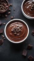 Rich chocolate mousse topped with chocolate chips in bowls on a dark surface with cocoa shards scattered around photo