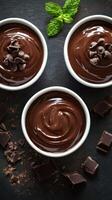 Rich chocolate mousse served in three bowls with chocolate chips and mint leaves on a dark surface photo