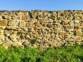 Rustic stone wall texture. Ancient, weathered masonry under a clear sky. Ideal for backgrounds, architectural designs, or historical projects. Evokes a sense of age and durability. photo