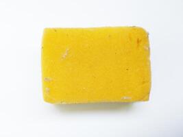 A wellused yellow cleaning sponge, slightly soiled, sits on a stark white background. photo