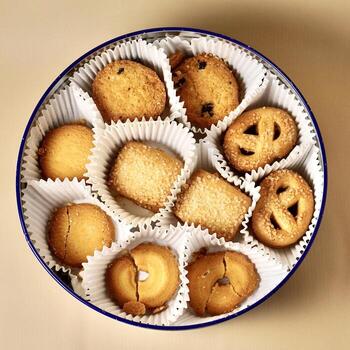 Yummy butter cookies with white paper cups in round container isolated on cream colored background from top angle view. photo