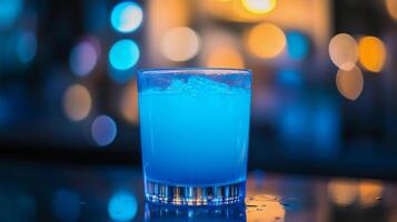 A glass of blue liquid is sitting on a table. The liquid is a bright blue color and he is a cocktail. The image has a cool, calming mood photo