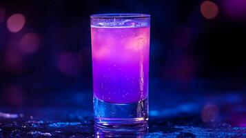 A purple drink in a glass is sitting on a table. The drink is purple and has a clear liquid in it photo