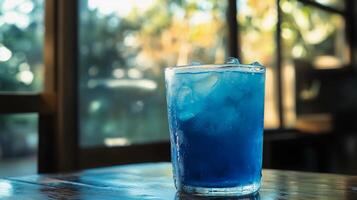 A glass of blue liquid with ice in it sits on a table. The glass is half full and the liquid is blue photo