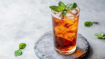 A glass of tea with a sprig of mint on top. The glass is half full and the mint is on the rim photo
