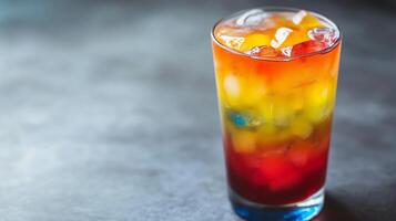 A glass of colorful drink with ice cubes in it. The drink is a mix of different colors and flavors photo