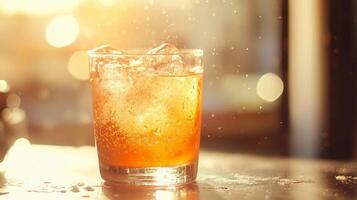 A glass of a drink with ice in it. The drink is a mixture of orange juice and soda. The glass is half full and the ice is melting, creating a splash. The image has a bright photo