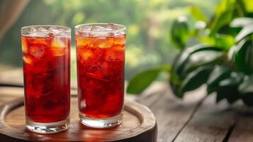 Two glasses of red drink on a wooden table. The drink is cold and refreshing. The table is made of wood and has a plant on it photo