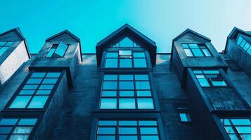 A row of tall buildings with large windows and a blue sky in the background. The buildings have a modern and sleek design, with a mix of brick and glass materials photo