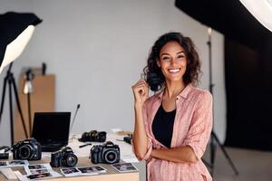 Smiling photographer poses confidently in her creative studio filled with diverse equipment and vibrant printed works photo