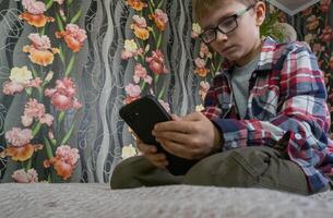 A boy on the sofa with a mobile phone in his hands. The boy is addicted to gadgets and uses a mobile phone at home. Internet obsession concept photo